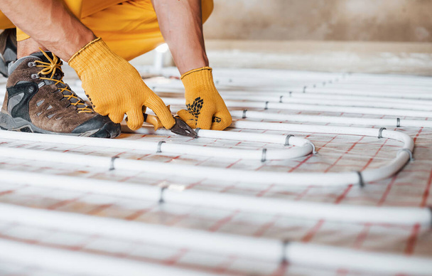 Close up view. Worker in yellow colored uniform installing underfloor heating system. - 写真・画像