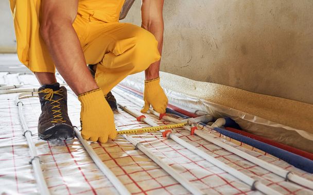 Measuring distance of the pipes. Worker in yellow colored uniform installing underfloor heating system. - Foto, Imagen