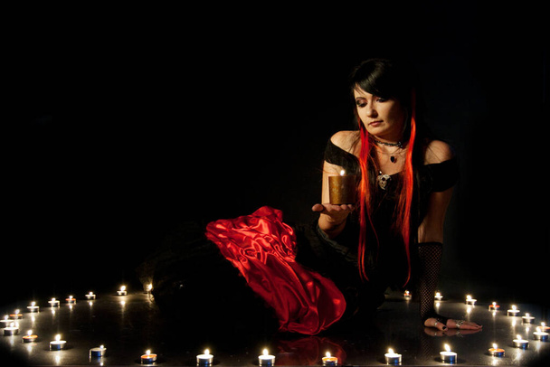 Belle jeune fille aux cheveux roux, portant une longue robe de flamenco gothique noire et rouge en dentelle avec corset noir. agenouillé sur le sol. isolé sur fond blanc. - Photo, image