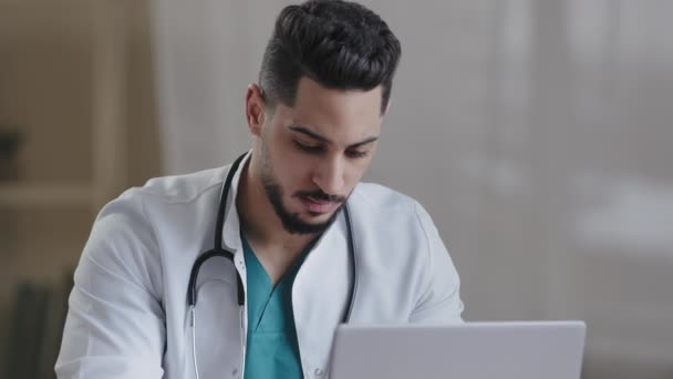 Skoncentrowany człowiek Latynoski lekarz lekarz nosić biały płaszcz używać komputera Internet w recepturze typu przepis dla pacjenta na komputerze w gabinecie szpitalnym mężczyzna młody stażysta skonsultować się zdalnie online czat medyczny - Materiał filmowy, wideo
