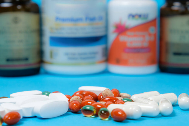 青の背景に白とオレンジのカプセルと錠剤、背景に栄養補助食品を持つ瓶 - 写真・画像