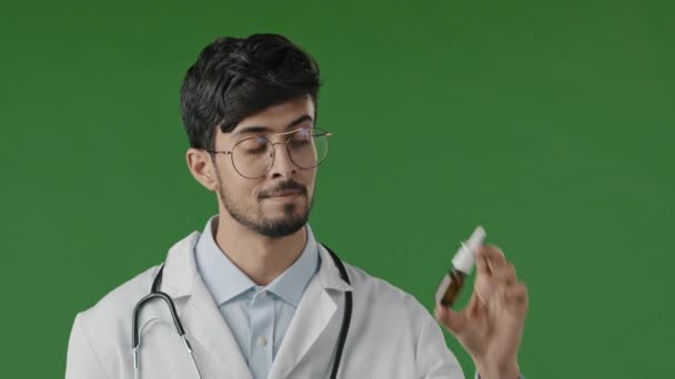 Árabe joven macho hispano médico indio en bata blanca aislado en estudio verde recomiendan en cámara nasal aerosol remedio líquido para la nariz la recuperación de los síntomas de alergia consejo de enfermedad publicidad - Imágenes, Vídeo
