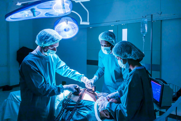 Zespół chirurga lekarz za pomocą defibrylatora do wstrząsu elektrycznego do serca pacjenta, który cierpi z powodu zatrzymania akcji serca w izbie przyjęć do zabiegu chirurgicznego koncepcji opieki zdrowotnej - Zdjęcie, obraz