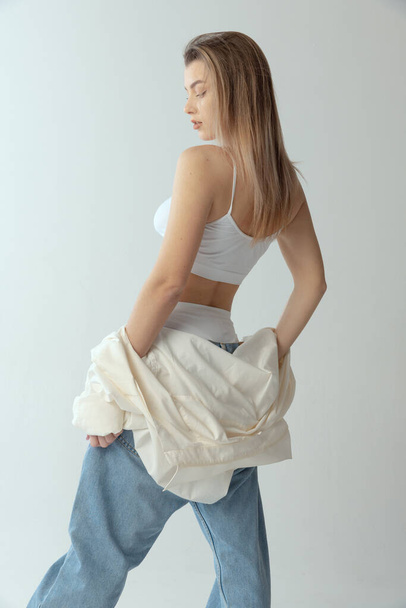Beautiful, stylish, slim girl wearing shirt, underwear and jeans posing isolated over grey studio backround. Side view - Φωτογραφία, εικόνα