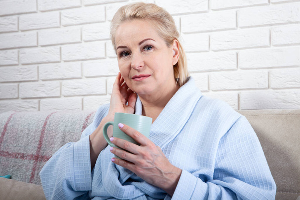 Happy beautiful middle aged woman drinking coffee on sofa at home - Foto, Imagen