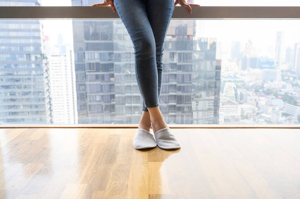 Detailní dámské sportovní džíny a pantofle stojící u plného okna. relaxace po pracovním dni, pohodlný obývací prostor. Kopírovat prostor - Fotografie, Obrázek