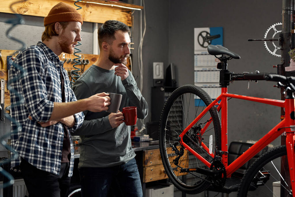 Thoughtful repairmen look at bicycle in workshop - Foto, afbeelding