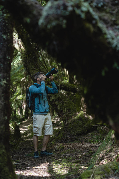 Man taking a photography with big lens among the trees of the wild forest. Vertical photography - Photo, Image