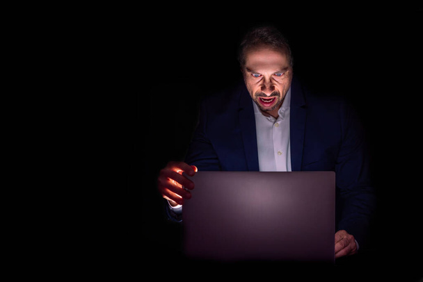 Wütender Mann vor seinem Laptop, im Dunkeln - Foto, Bild