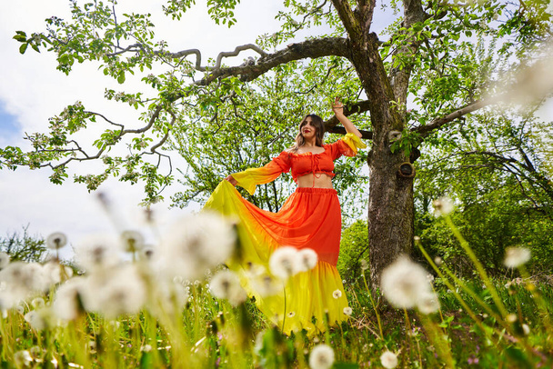 Beautiful young indian woman in long orange dress in an apple orchard - Фото, зображення