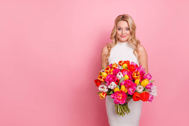 Photo of cheerful positive woman wear white dress getting flowers bunch empty space isolated pink color background - Zdjęcie, obraz