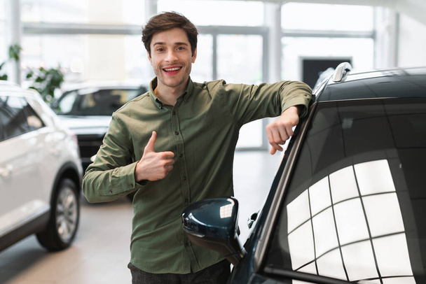 Positive millennial Caucasian guy showing thumb up gesture, recommending selection of automobiles at dealership store - Photo, Image