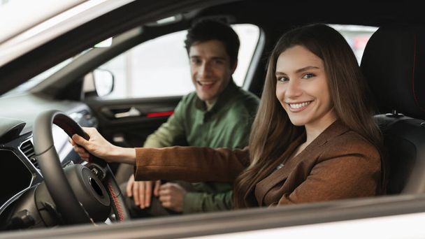 Веселая молодая пара сидит внутри нового автомобиля, проверяя его перед покупкой в дилерском магазине, баннер дизайн - Фото, изображение