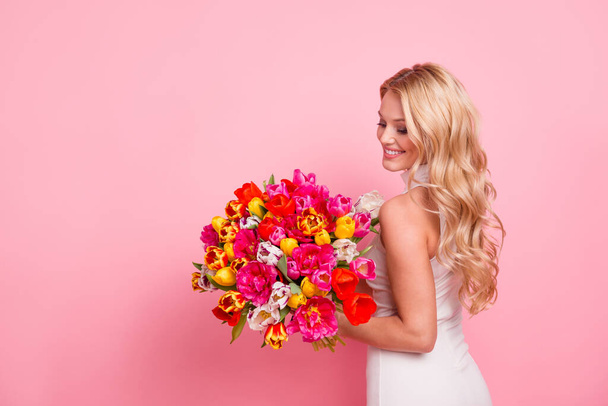 Photo of cheerful sweet woman wear white dress holding flowers bunch empty space isolated pink color background - 写真・画像