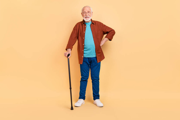 Photo of pretty funny guy pensioner dressed brown shirt glasses holding walking cane isolated beige color background - 写真・画像