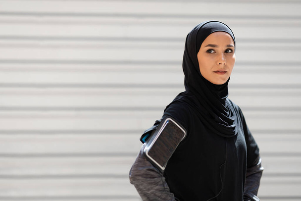 Αυτοπεποίθηση σοβαρή ηρεμία όμορφη νεαρή μουσουλμάνα γυναίκα σε μαντίλα με το τηλέφωνο στον ώμο της ανάπαυση από τις ασκήσεις - Φωτογραφία, εικόνα