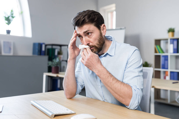 Businessman sick in the office man with allergies sneezes, sitting at a table with a computer - Photo, Image