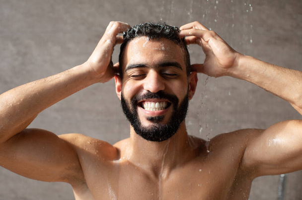 Happy handsome young Arabic male model taking hot shower - Photo, Image
