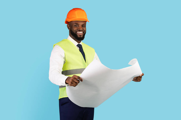 Smiling African American Contractor Holding Blueprints While Standing Isolated Over Blue Background - Fotografie, Obrázek