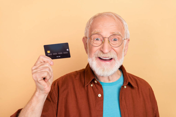 Photo of hooray old grey hairdo man hold card wear spectacles brown shirt isolated on beige color background - Foto, afbeelding