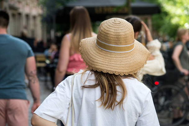 Portrait on back view of young woman wearing a summer hat walking in the street - Фото, изображение