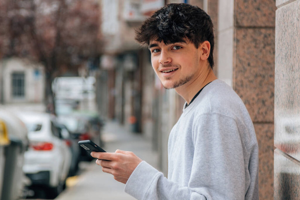νεαρός έφηβος χιλιετή χρησιμοποιώντας το κινητό τηλέφωνο ή το smartphone στο δρόμο της πόλης - Φωτογραφία, εικόνα