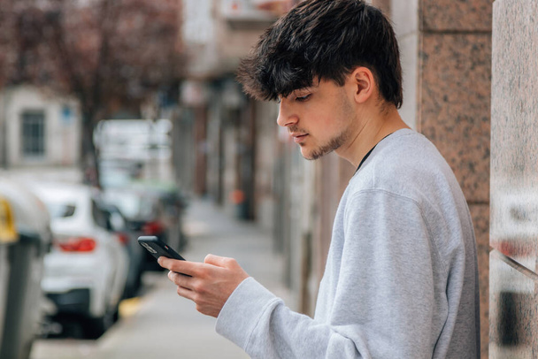 Jeune adolescent millénaire utilisant un téléphone mobile ou un smartphone dans la rue de la ville - Photo, image