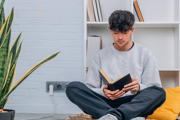 έφηβος φοιτητής στο σπίτι ή βιβλιοθήκη διαβάζοντας ένα βιβλίο ή μελετώντας - Φωτογραφία, εικόνα