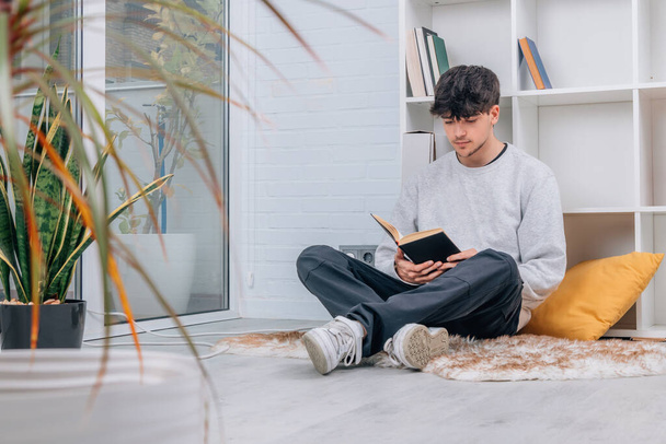 nastolatek w domu lub bibliotece czytający książkę lub studiujący - Zdjęcie, obraz