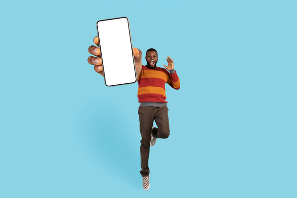 陽気な興奮黒男性ジャンプとともにビッグブランク携帯電話で手 - 写真・画像