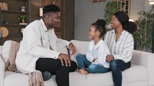 リビングルームでソファに座っているアフリカ系アメリカ人の家族は、カジュアルな会話笑いをチャット。新しい子供の娘養子とのコミュニケーションを話す出生多人種保護者家庭で女の子を採用 - 映像、動画