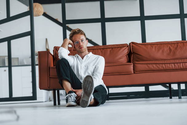 Having a rest. Caucasian young guy in elegant white shirt indoors at home. - Foto, Bild