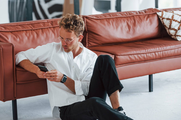 Having a rest. Caucasian young guy in elegant white shirt indoors at home. - Φωτογραφία, εικόνα
