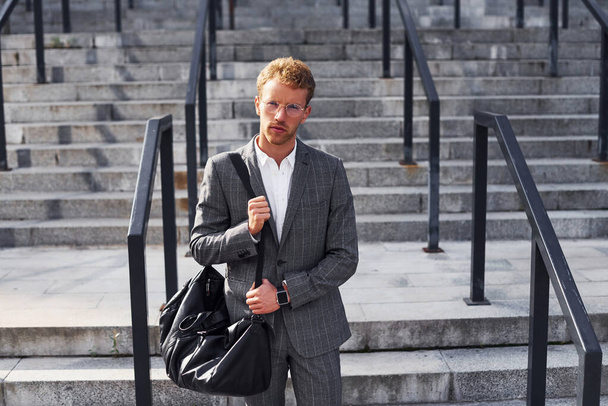 Young successful businessman in grey formal wear is outdoors in the city. - Фото, зображення