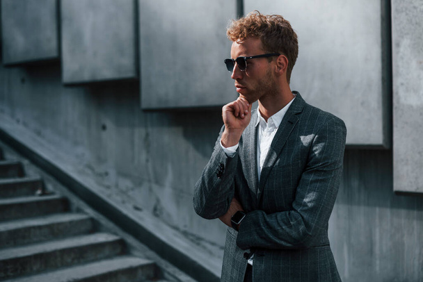 Young successful businessman in grey formal wear is outdoors in the city. - Fotoğraf, Görsel