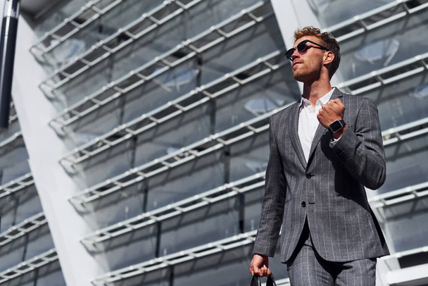 Celebrating success. Young businessman in grey formal wear is outdoors in the city. - Fotoğraf, Görsel