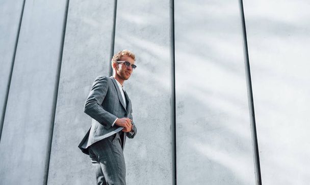 In sunglasses. Young successful businessman in grey formal wear is outdoors in the city. - Foto, Imagen