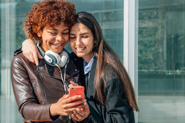 Mädchen lächeln auf der Straße und schauen auf das Handy - Foto, Bild