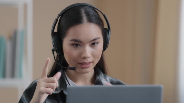 Aasian naispuolinen toimistotyöntekijä käyttää kuulokkeita on kaukainen konferenssi videopuhelu kannettavan tietokoneen kanssa. Korean liikenainen asiakaspalvelupäällikkö asiakas neuvontapuhelin agentti online-palvelu puhuu webcam - Materiaali, video