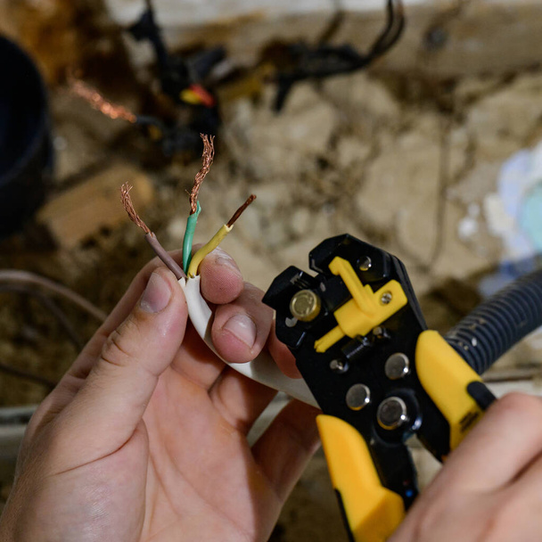 Zastosowanie narzędzia do usuwania izolacji w celu usunięcia końca przewodu elektrycznego podczas naprawy i aktualizacji okablowania elektrycznego w domowej sieci elektrycznej, prace elektryczne, kabel elektryczny. - Zdjęcie, obraz