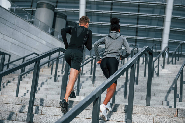 Running on bleachers. European man and african american woman in sportive clothes have workout together. - Foto, immagini
