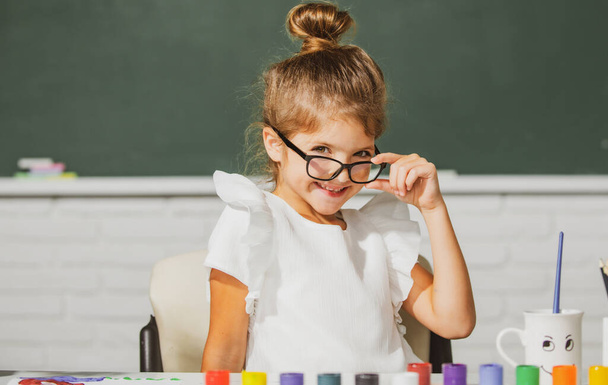 Cute school girl face with glasses. Little girls drawing a colorful pictures with pencil crayons in school classroom. Painting kids. - Photo, image
