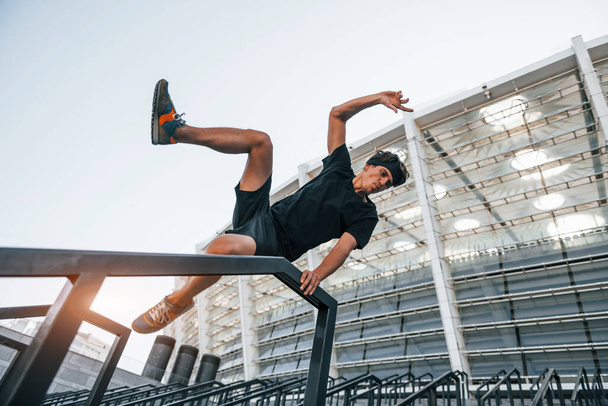Does parkour. Young man in sportive clothes have workout outdoors at daytime. - Foto, imagen