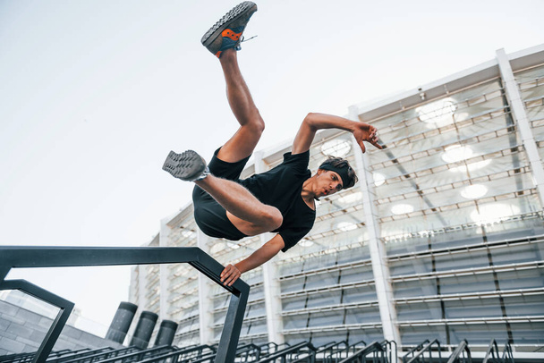 Does parkour. Young man in sportive clothes have workout outdoors at daytime. - 写真・画像