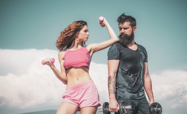 Building up muscle. Couple of athletes doing muscle training with dumbbells. Fit woman and strong bearded man developing muscle tissue. Sexy woman and hipster doing muscle strengthening exercises - Foto, afbeelding