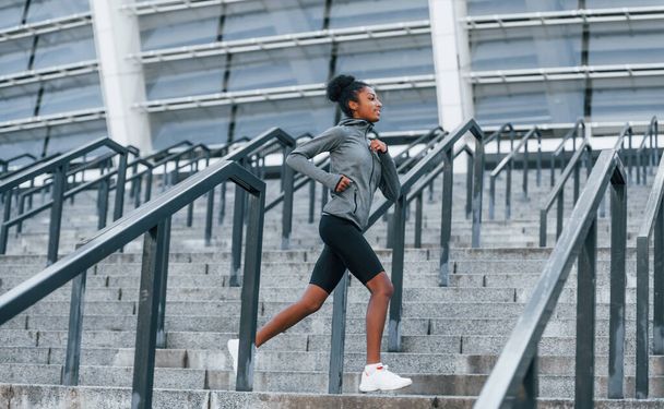 Active runner. Young african american woman in sportive clothes have workout outdoors at daytime. - Foto, imagen