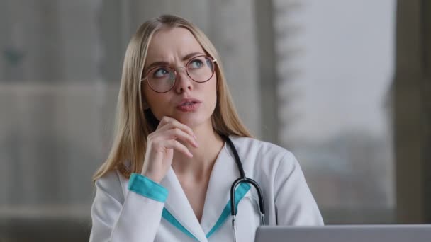 Focused caucasian female pensive nurse smart woman practitioner doctor thinking of problem diagnosis appointment solution makes decision comes up with idea typing laptop online advice to patient - Video