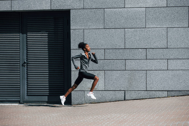 Side view of young african american woman in sportive clothes that runs near wall. - Foto, Bild
