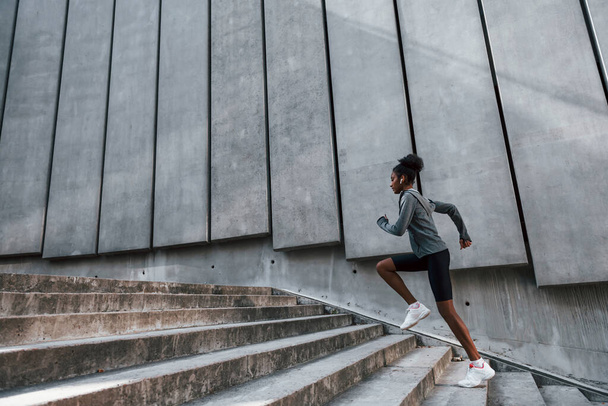 Fast runner. Young african american woman in sportive clothes have workout outdoors at daytime. - 写真・画像