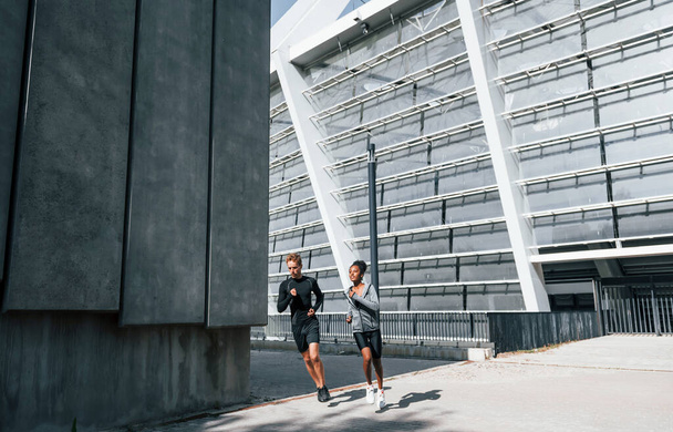 Near big wall. European man and african american woman in sportive clothes have workout together. - Photo, image